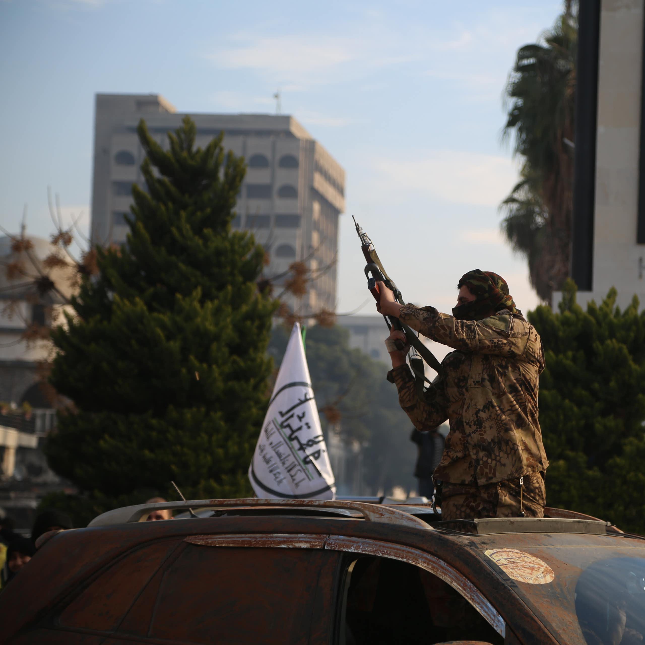 A Syrian rebel holding a gun aloft through the roof of a car.