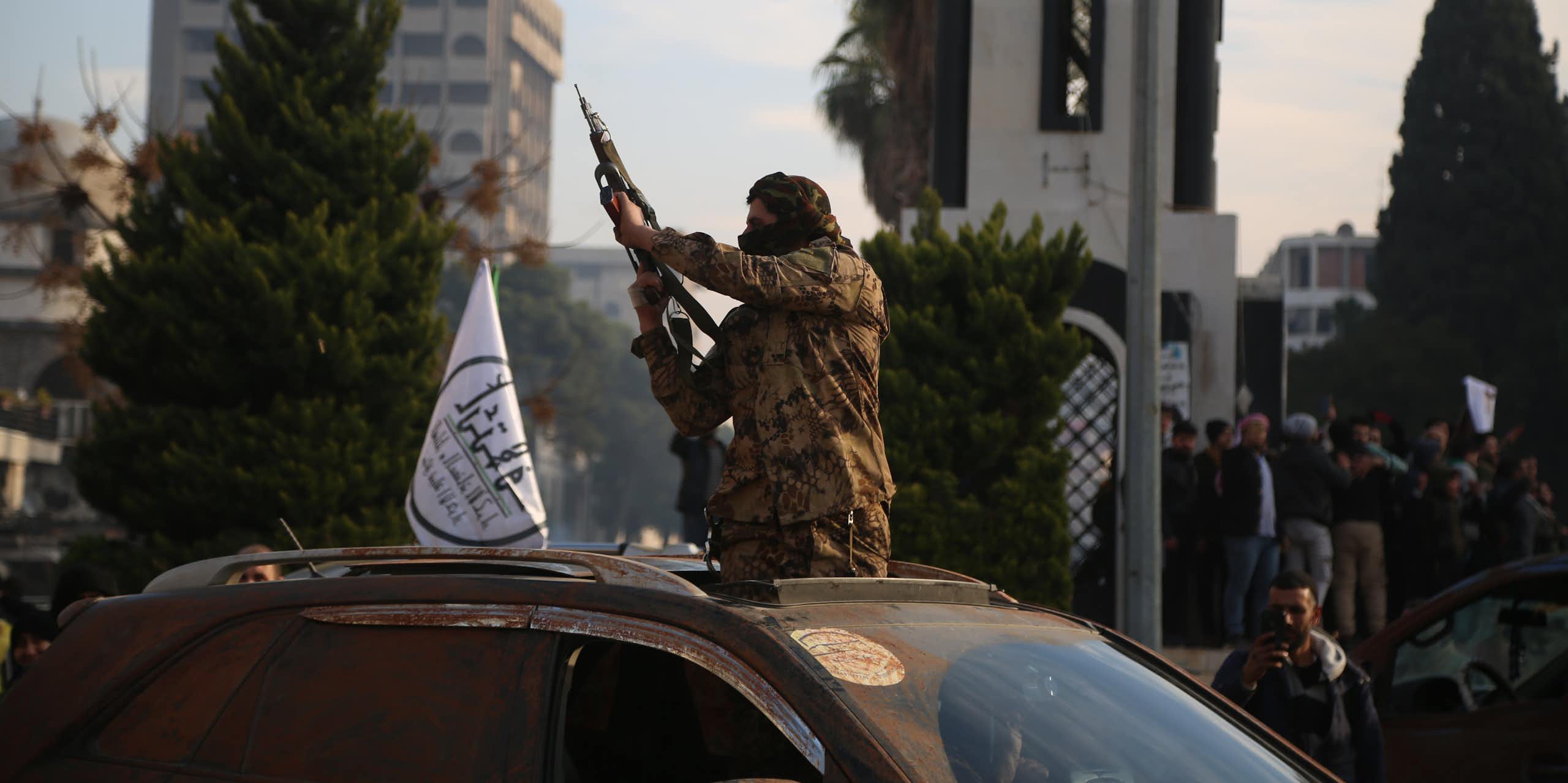A Syrian rebel holding a gun aloft through the roof of a car.