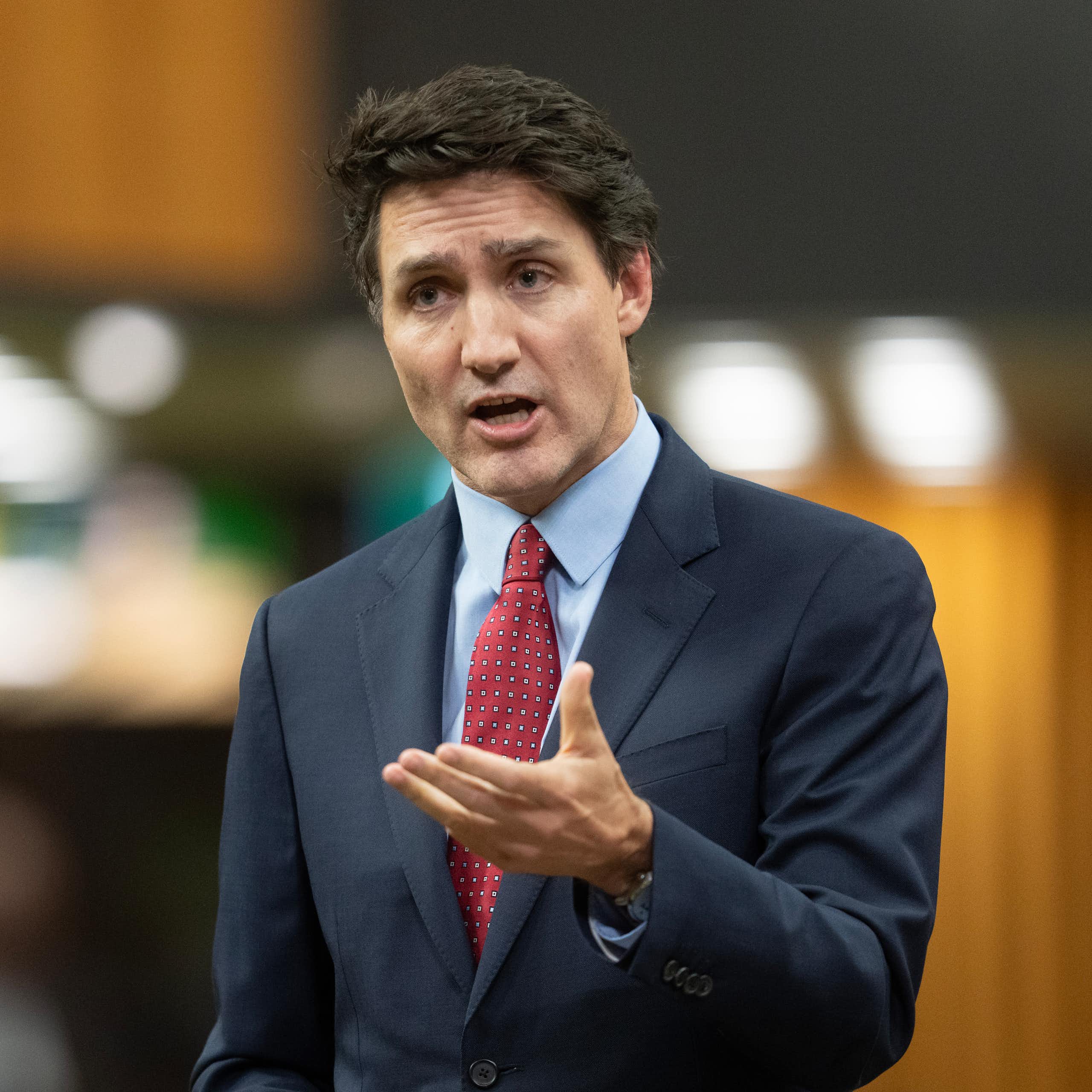 A middle-aged white man in a navy suit and red tie gestures with one hand while speaking
