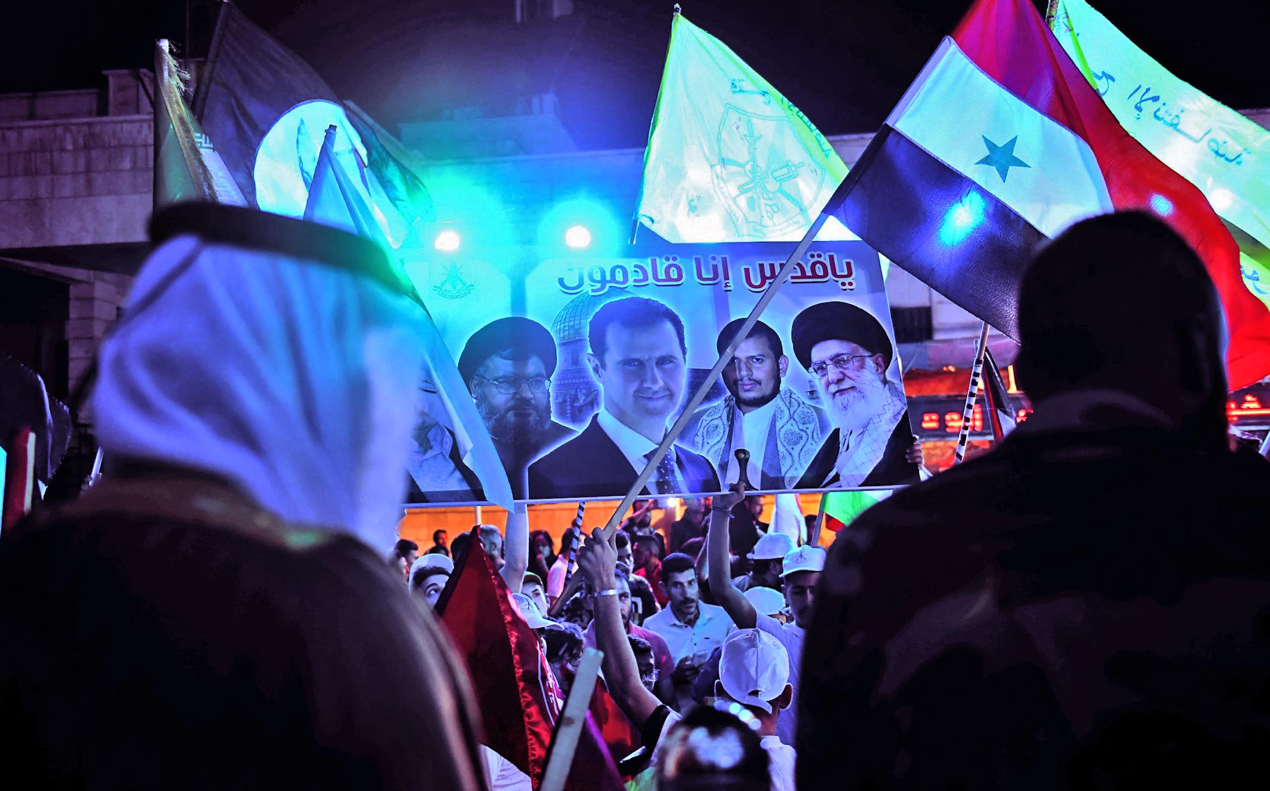 Men wave flags and a banner showing the face of four men.