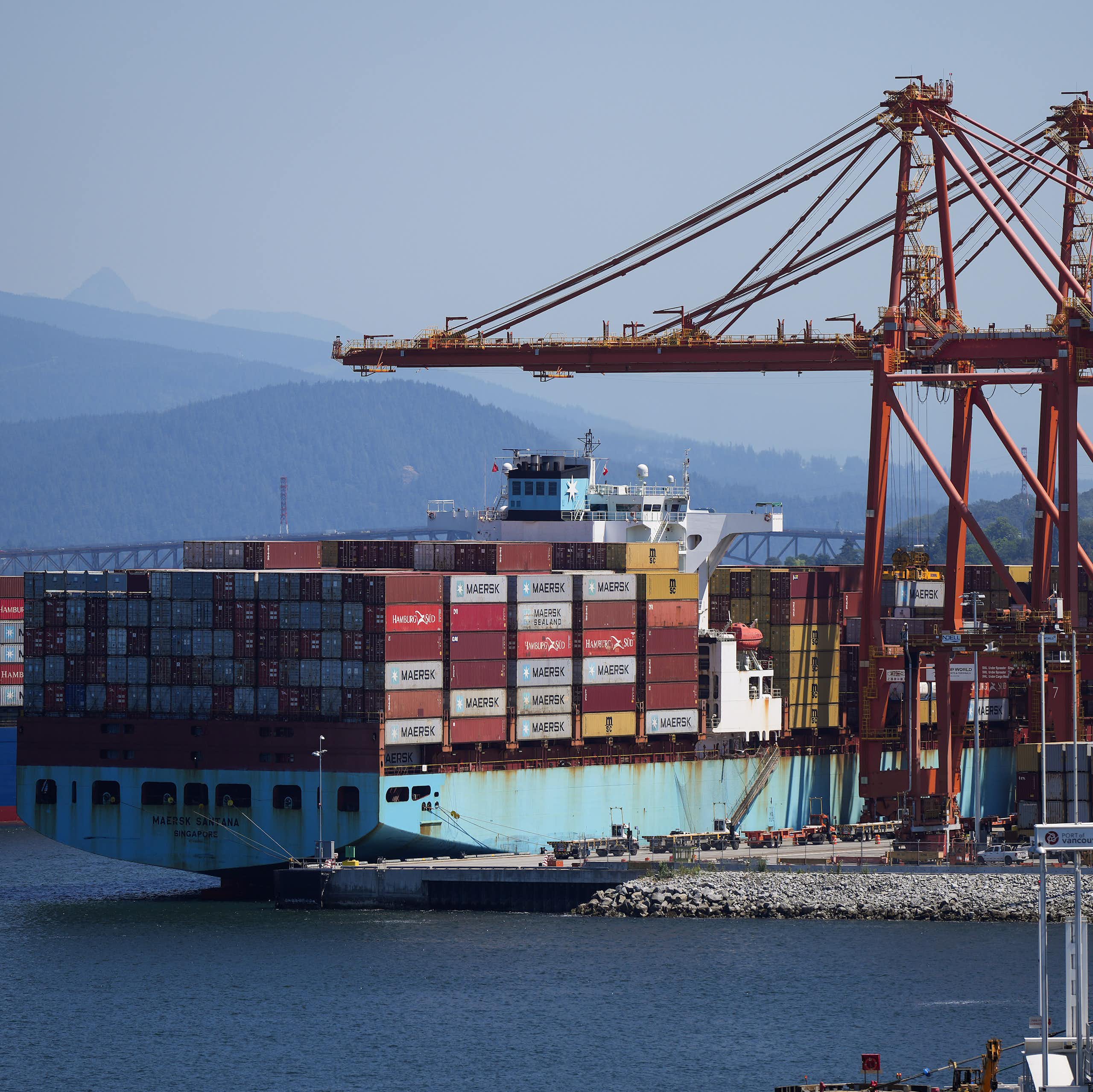 A huge cargo ship laden with shipping contains sits in front of a dock