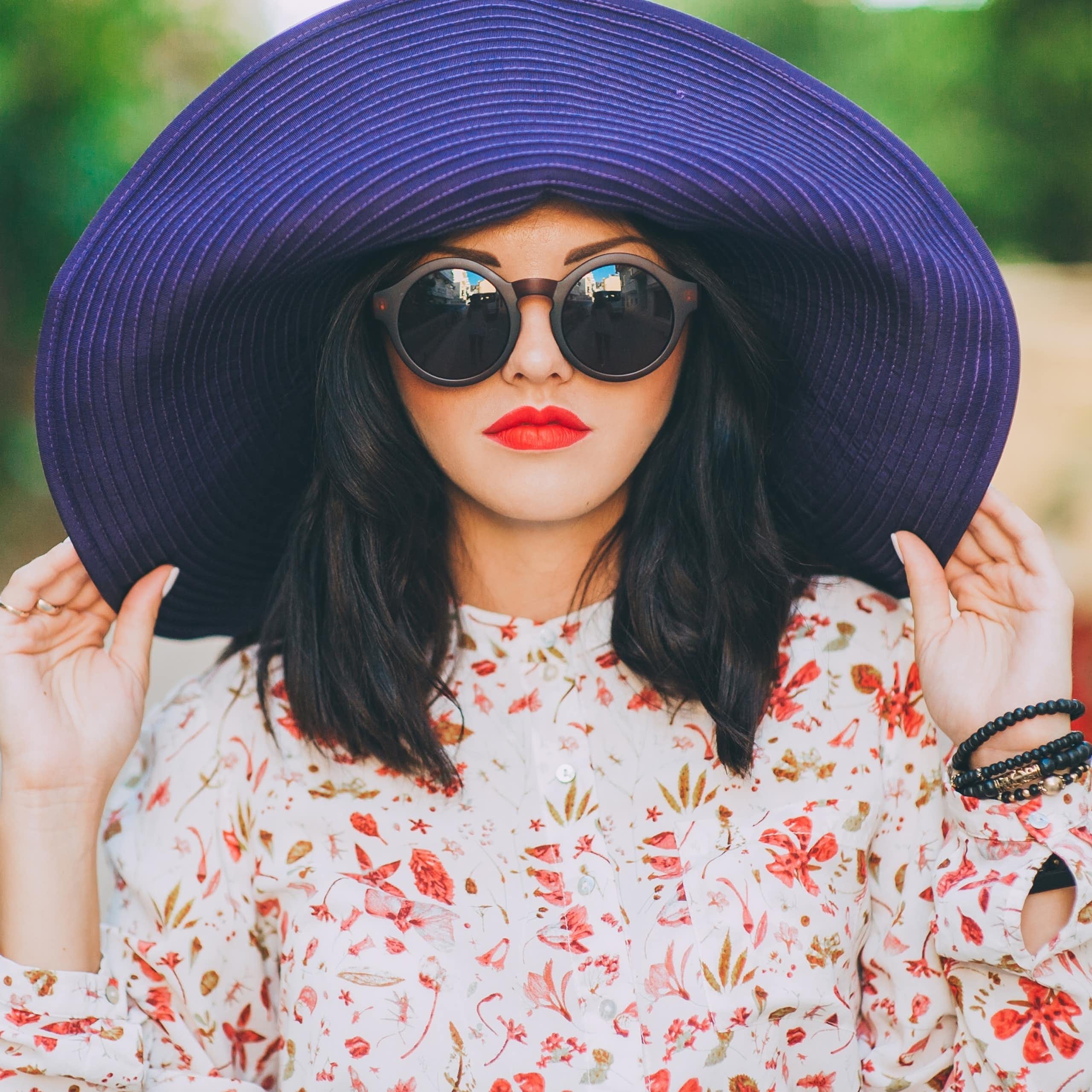A fashionable woman wears sunglasses and a big hat.