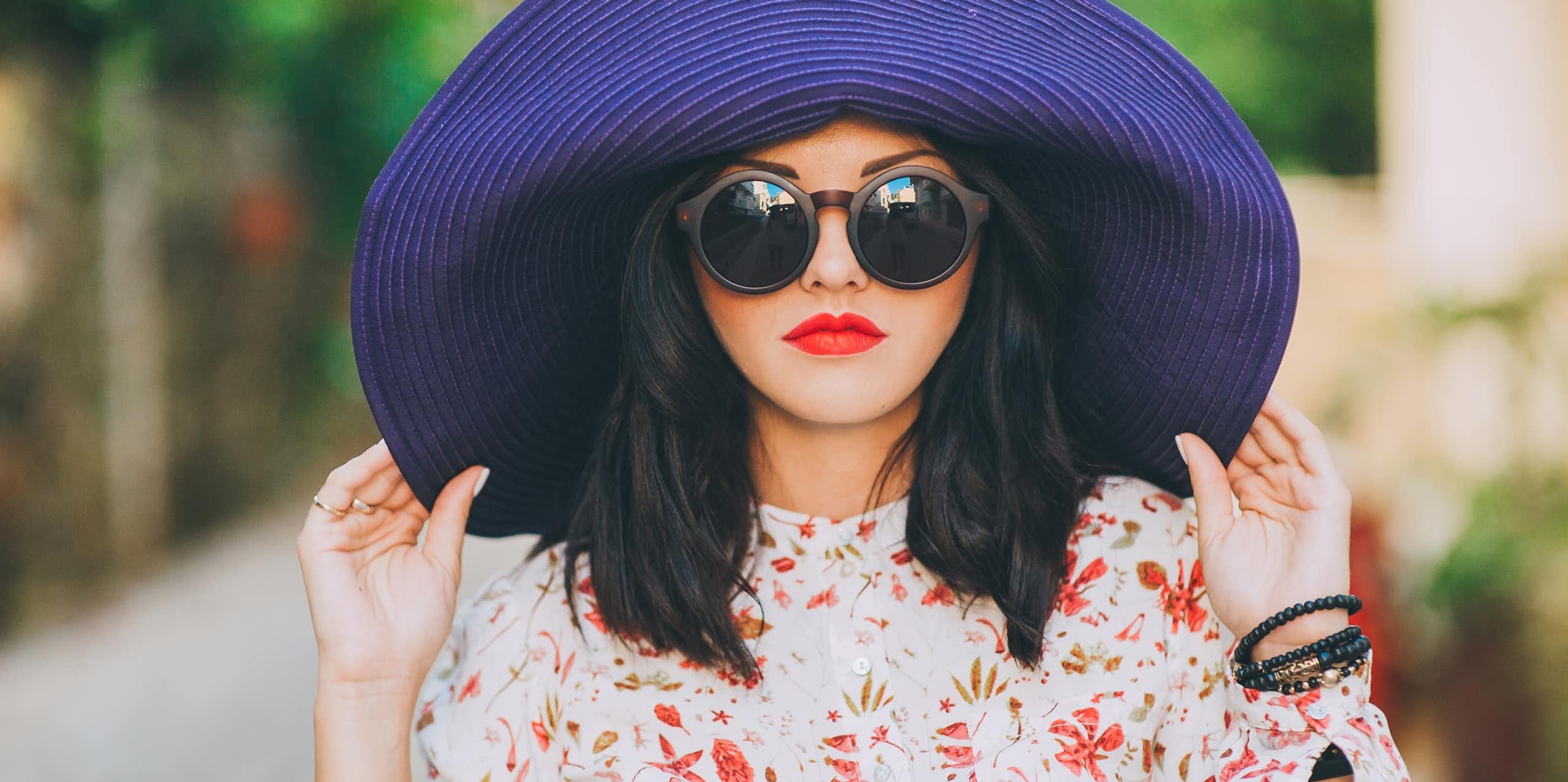 A fashionable woman wears sunglasses and a big hat.
