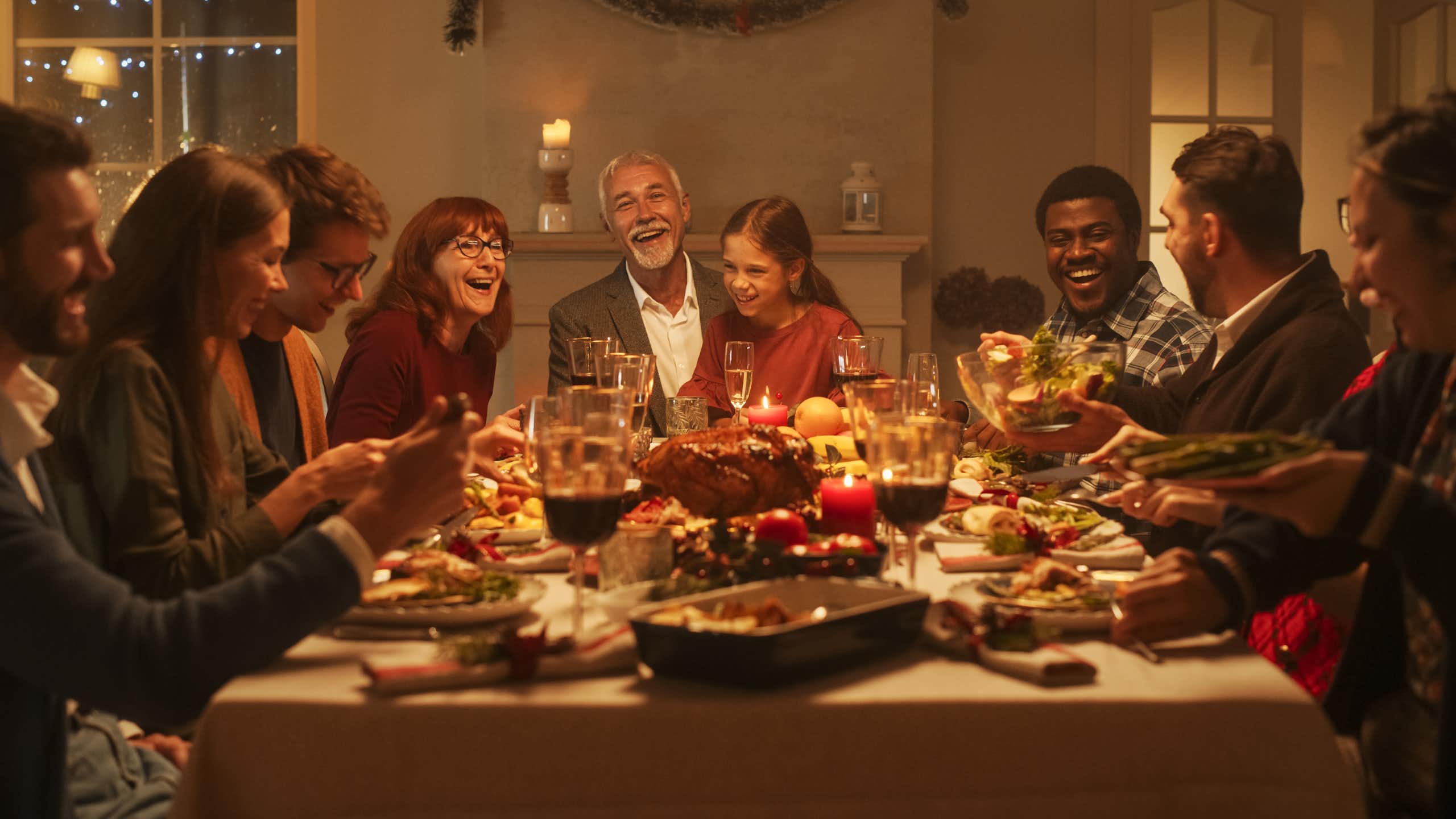 Un groupe de huit personnes sont assises et sourient devant une table remplie de nourriture et de verres de vin 