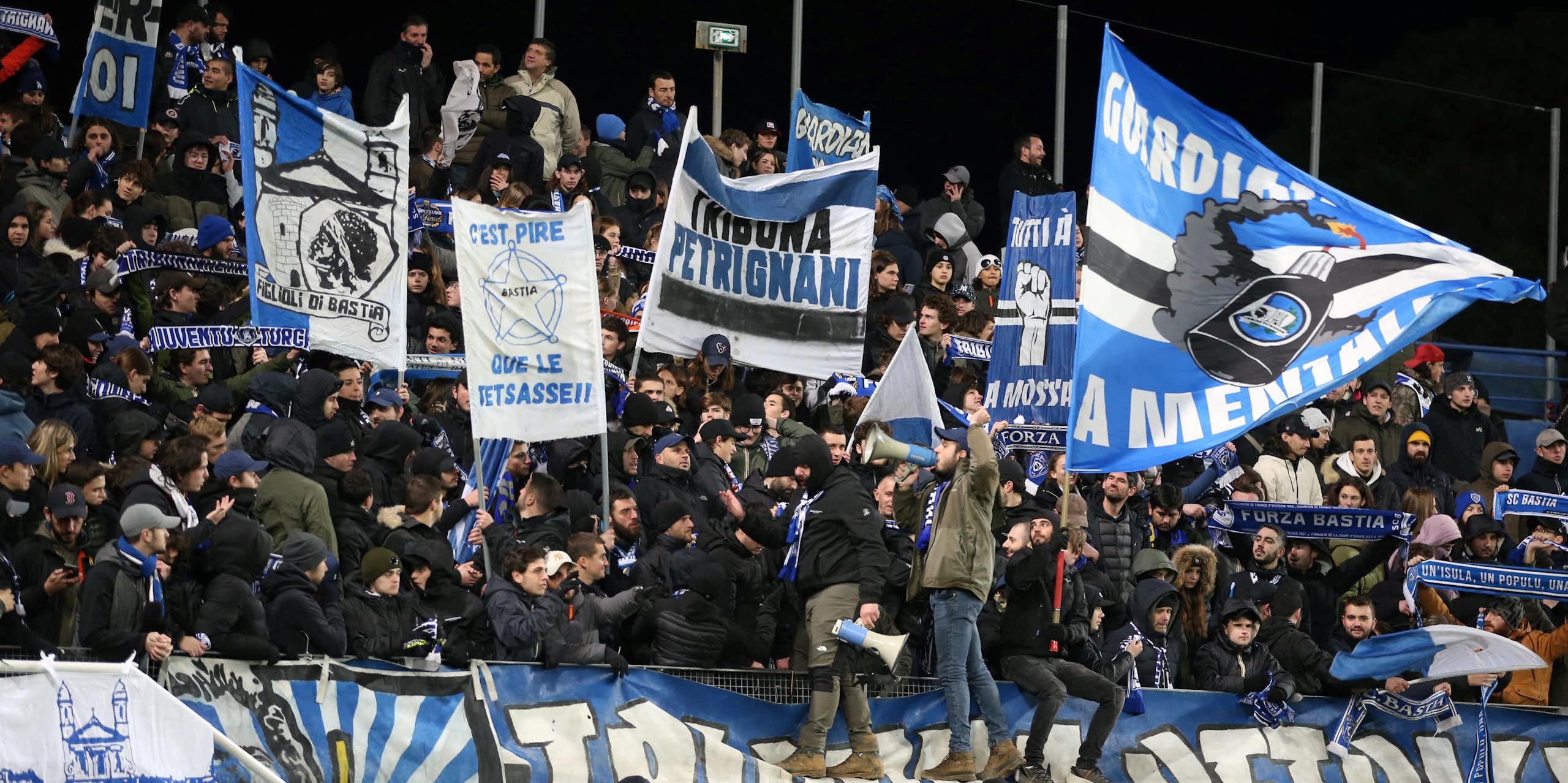 Des supporters agitent des drapeaux depuis les tribunes d'un match de football.