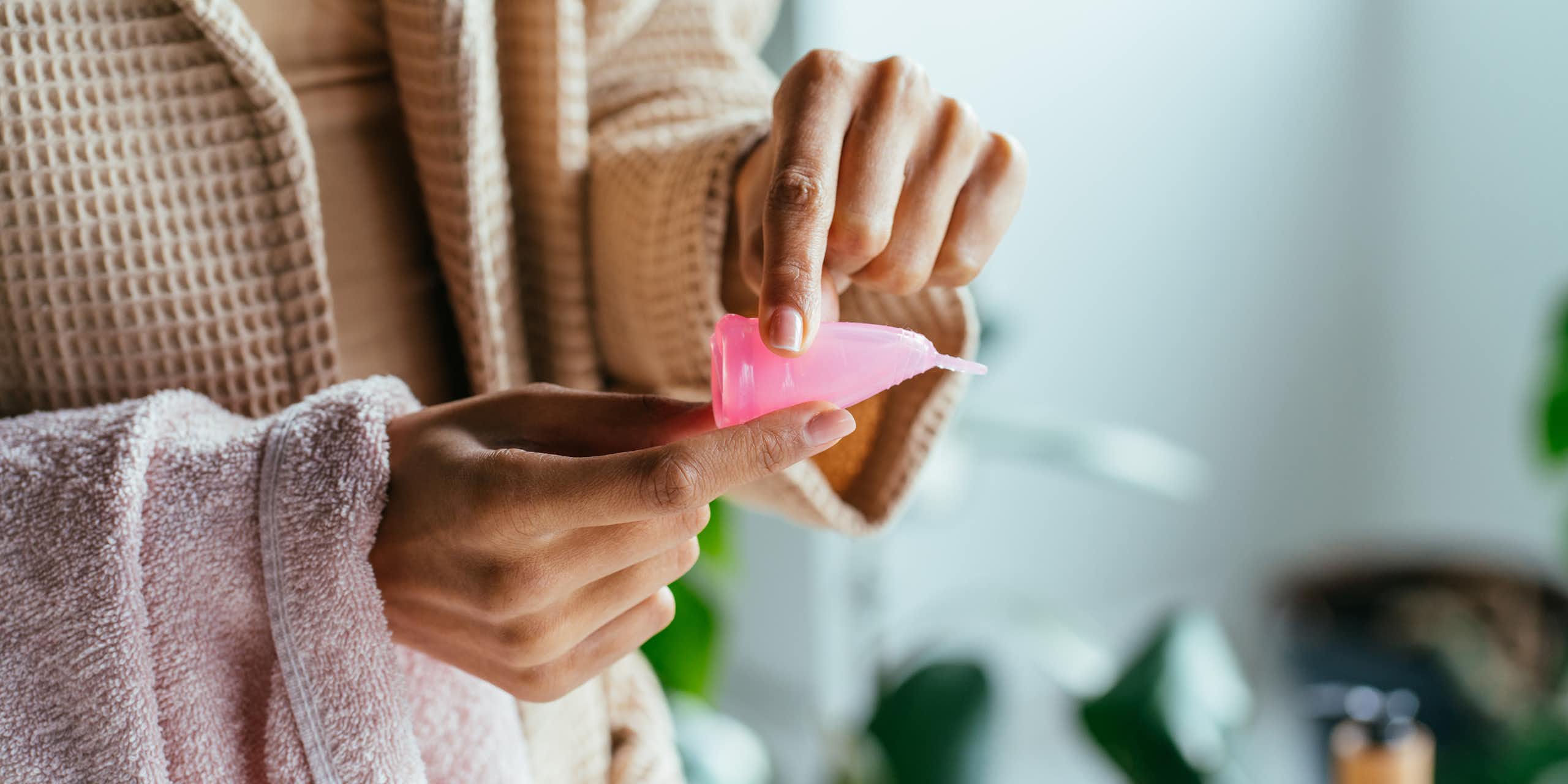 A woman bending a pink menstrual cup.