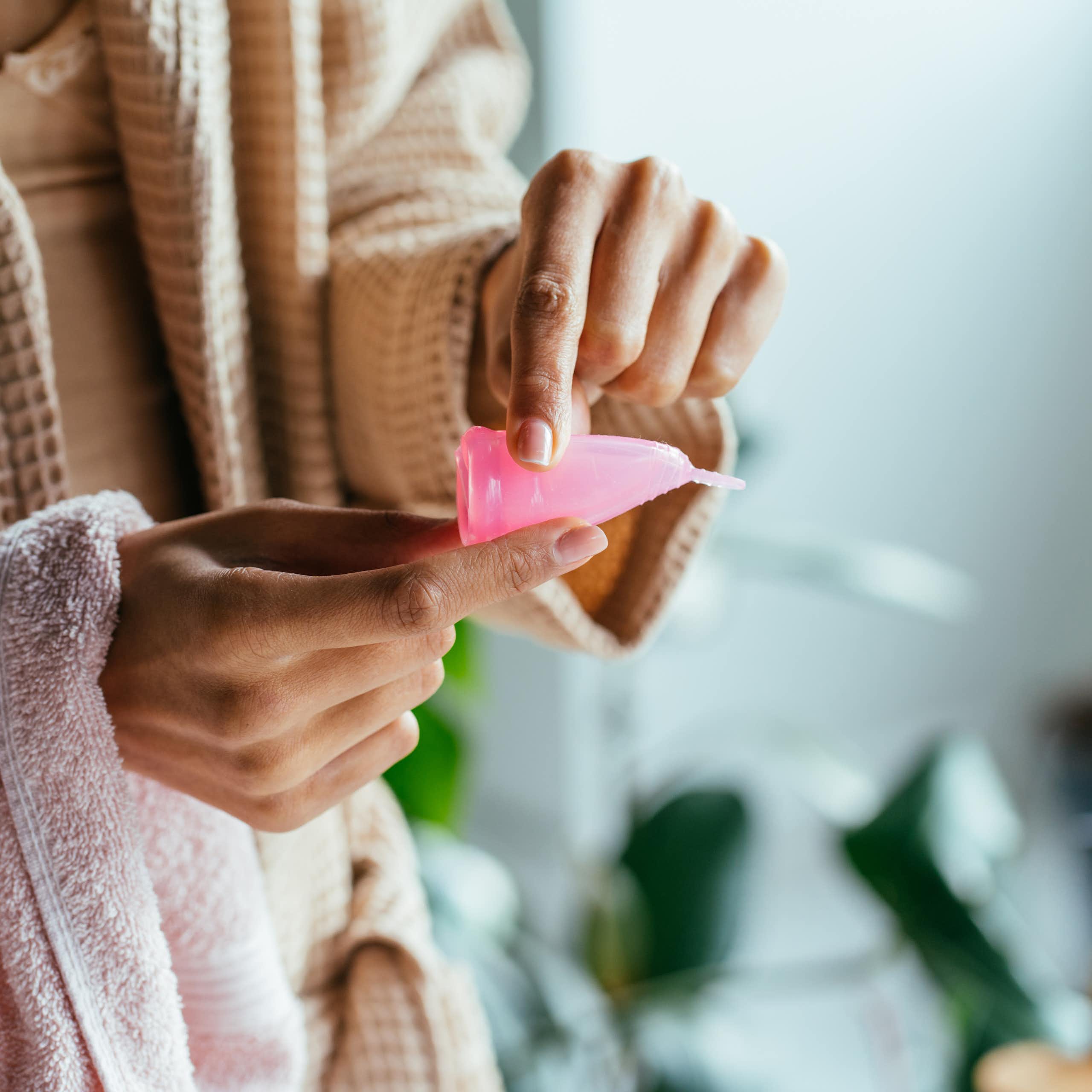 A woman bending a pink menstrual cup.