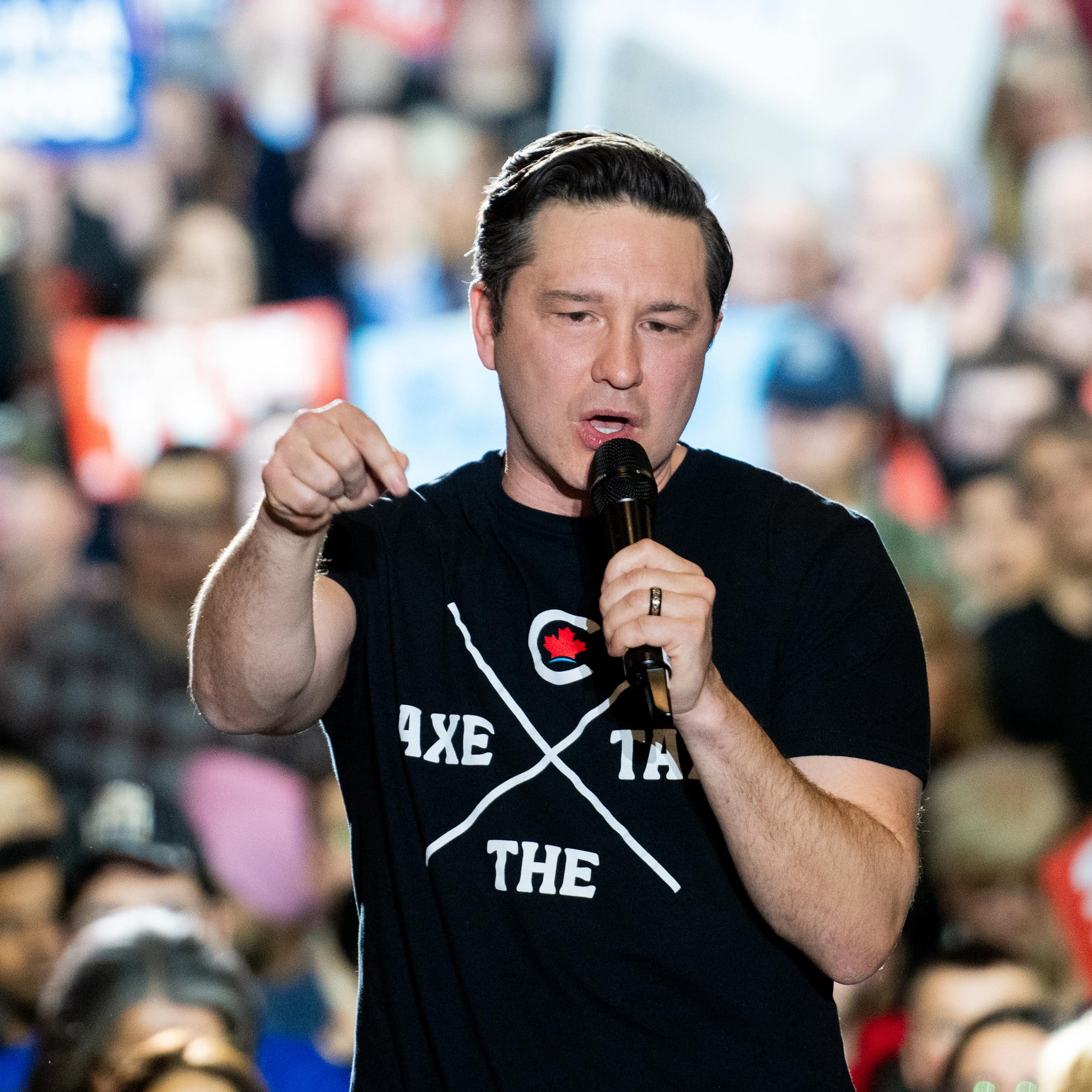 A man in a t-shirt talks into a microphone in front of a crowd.
