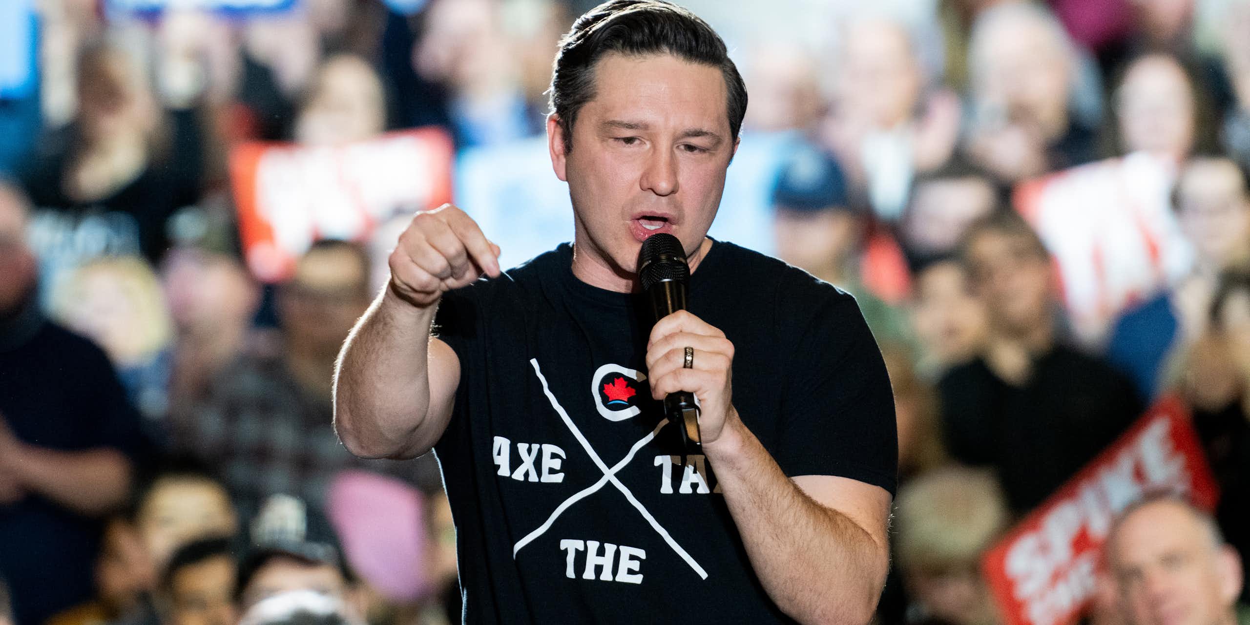 A man in a t-shirt talks into a microphone in front of a crowd.