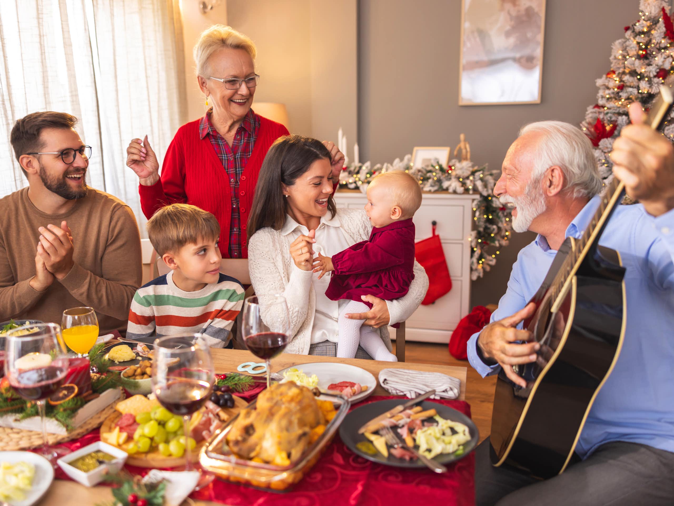 Un homme âgé joue de la guitare lors d'une soirée de Noël en famille sous le regard faussement extatique de ses proches.